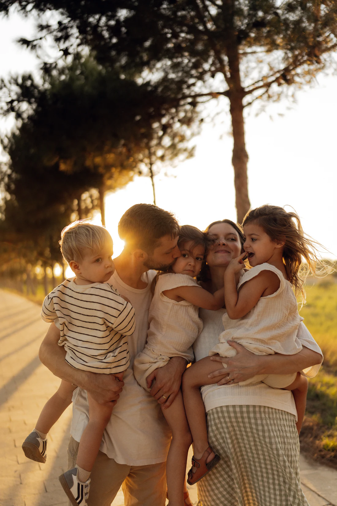 Parents and three children laughing under backlit trees